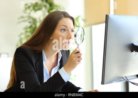 Sospettoso lavoratore di ufficio controllo contenuti online sul computer utilizzando una lente di ingrandimento Foto Stock