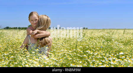 Carino bambina abbracciando la sua mamma sul prato fiorito, cielo blu in background Foto Stock