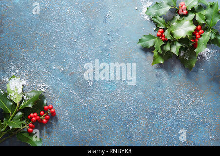 Sfondo di natale con real holly foglie e bacche di colore rosso su una pietra blu sullo sfondo coperto di neve con copia spazio. Foto Stock