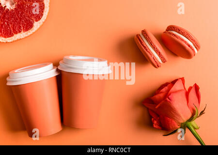 Coral bicchieri di carta, rose fiore, macarons e pompelmo metà su sfondo di corallo, il colore del concetto 2019 Foto Stock