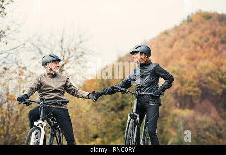 Attivo coppia senior con electrobikes in piedi all'aperto su una strada in natura. Foto Stock