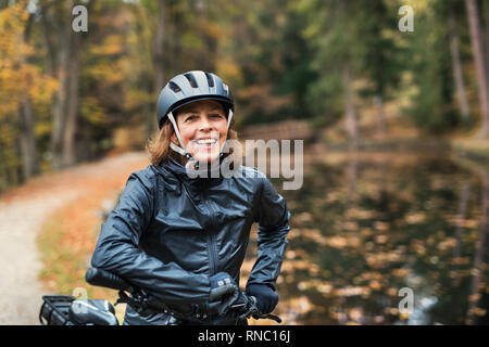 Un senior donna con electrobike in piedi all'aperto su una strada nel parco in autunno. Foto Stock