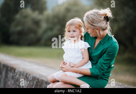Giovane madre in natura con la piccola figlia, seduto su un muro di pietra. Foto Stock