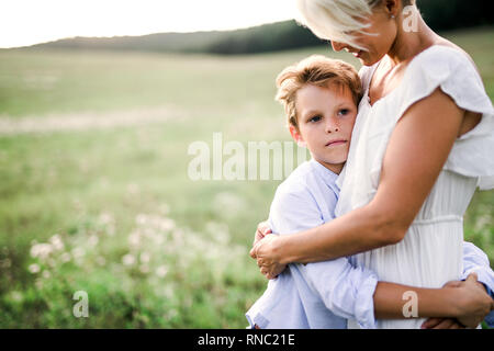 Un piccolo ragazzo abbraccia il suo giovane madre all'aperto in natura. Foto Stock