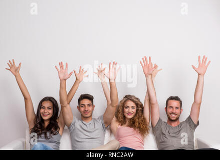 Ritratto di giovane gruppo di amici seduti su un divano in un studio, braccia verso l'alto. Foto Stock