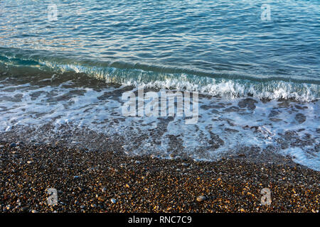 Una piccola onda corre sulla spiaggia di sabbia morbida in mattinata raggi del sole. Foto della costa nelle prime ore del mattino. Il concetto di vacanze estive Foto Stock