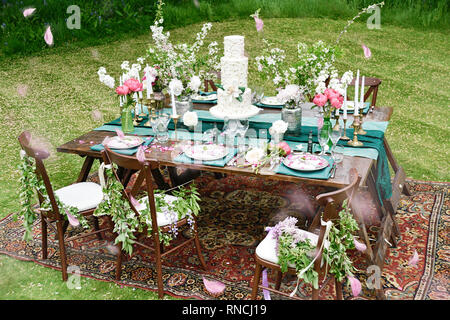 Un bellissimo tavolo esterno display, con un sacco di fiori di primavera in vari colori- situato in un verde giardino erboso su un luminoso giorno Foto Stock