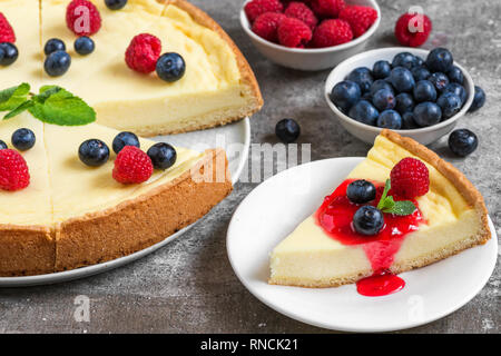 Classic fette di New York cheesecake con frutti di bosco freschi e marmellata su sfondo di pietra, vicino. ottima colazione Foto Stock