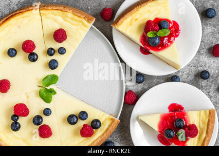 Cheesecake con due fette di torta con lamponi freschi, mirtilli, marmellata e menta su calcestruzzo sfondo. vista dall'alto. gustosa prima colazione Foto Stock