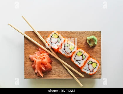 Bastoncini con la California sushi rotoli maki, wasabi e zenzero su una lastra di legno con sfondo grigio - il cibo giapponese e cultura Foto Stock