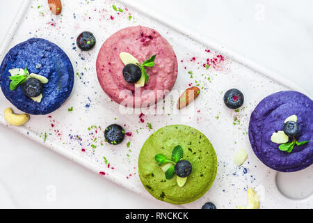 In casa materie vegan torte colorate con matcha, acai e butterfky pea tè, frutti di bosco freschi, menta, dadi. sano cibo vegan concetto. vista superiore. laici piatta Foto Stock