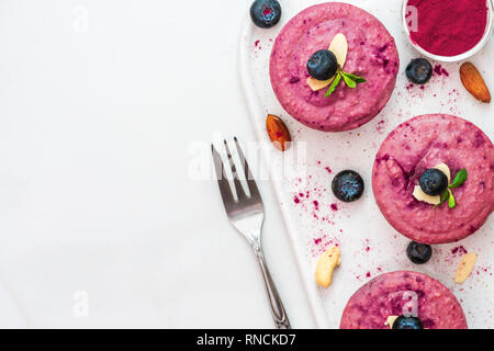 Materie mirtillo e acai vegan cheesecake con frutti di bosco freschi, menta, dadi e forcella. sano cibo vegan concetto. vista superiore. laici piatta Foto Stock