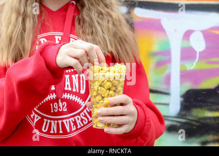 Giovane ragazza tenendo un barattolo di popcorn dorato contro il muro di graffiti nel parco Foto Stock