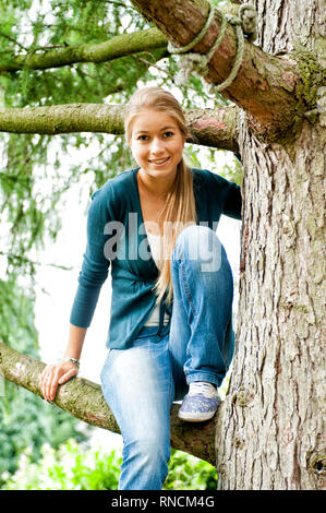 Junge Frau mit langen Haaren blondn sitzt auf einem Baum [(c) Dirk A. Friedrich Foto Stock