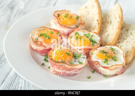 Uova e pancetta tazze con fette di pane abbrustolito sulla piastra bianca Foto Stock