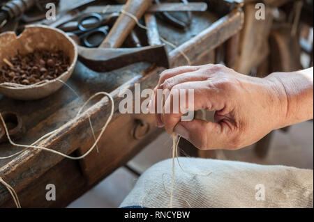 Il calzolaio prepara la stringa per la cucitura di una calzatura. Vari strumenti e lo strumento sono collocati sul banco di lavoro Foto Stock