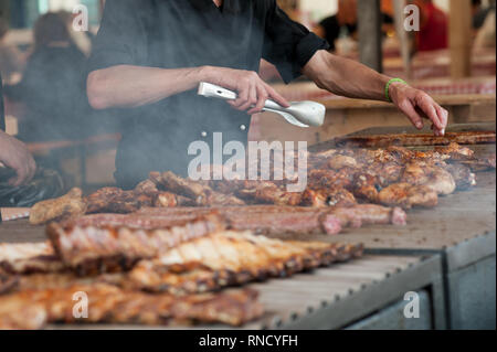 L'uomo la cottura alla griglia di un assortimento di carni di pollo e su un grande barbecue Foto Stock