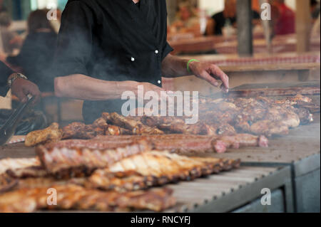 L'uomo la cottura alla griglia di un assortimento di carni di pollo e su un grande barbecue Foto Stock