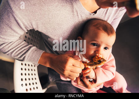 Bambino di 4 mesi rodendo un pollo gamba, degustando i suoi primi alimenti utilizzando il metodo dei led del bambino allo svezzamento BLW. Foto Stock