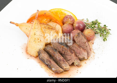 Un filetto di piccione singolo, grigliato e tagliato a fette servito con pere, arance, uva e mele che sono state delicatamente fritte nel burro aromatizzato con fres Foto Stock