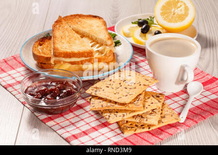 Fette biscottate di pane con formaggio, i cookie con grani interi di semi di girasole, tagliare il limone sulla piastra, una tazza di caffè e la ciotola di vetro con fragola ja Foto Stock