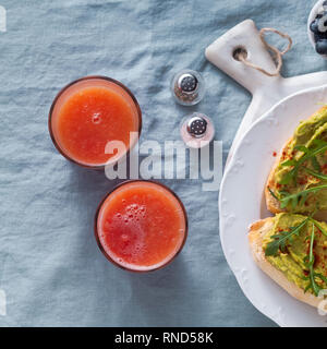 Avocado e rucola sandwich con paprika sul tavolo. sana colazione o uno spuntino su una piastra su un lino blu tovaglia e spremute grapefru Foto Stock