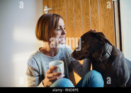 Una giovane donna seduta al chiuso sul pavimento a casa, giocando con un cane. Foto Stock