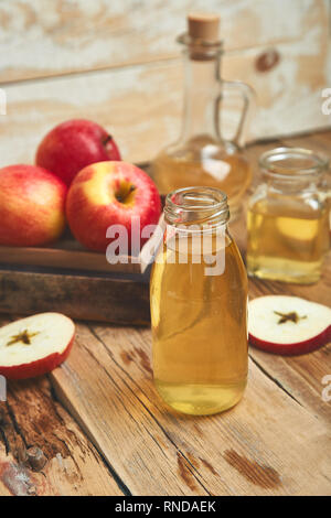 Apple di aceto di sidro. Bottiglia di vetro di apple aceto organico su un tavolo di legno. Organico sano bere cibo. Bottiglia di sidro fresco nei pressi di autunno le mele rosse. Foto Stock