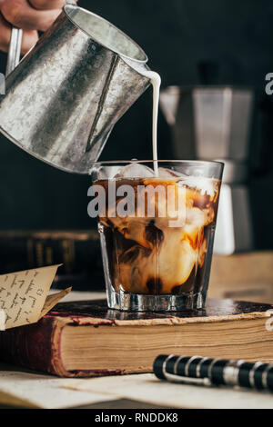 Versare il latte in un caffè freddo il vetro Foto Stock