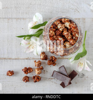 Popcorn al cioccolato e pezzi di cioccolato e fiori su un tavolo di legno Foto Stock