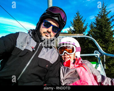 Famiglia godendo le vacanze invernali tenendo selfie in marcia di sci. Padre e figlia su sciare vacanza vestito su sci lift con i caschi e occhiali da sci Foto Stock