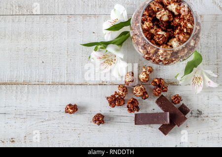 Popcorn al cioccolato e pezzi di cioccolato e fiori su un tavolo di legno Foto Stock