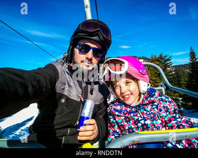 Famiglia godendo le vacanze invernali tenendo selfie in marcia di sci. Padre e figlia su sciare vacanza vestito su sci lift con i caschi e occhiali da sci Foto Stock