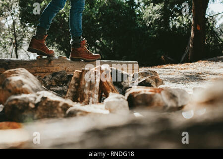 Basso angolo di vista di una persona che cammina su un albero caduto trunk in una foresta. Tagliate il colpo di una persona che indossa scarpe di cuoio a piedi nella foresta. Foto Stock