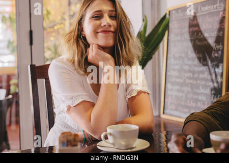 Felice giovane donna seduta al cafe con il suo amico. Rilassante seduta femminile presso la caffetteria con un amico maschio. Foto Stock