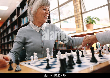 Senior donna giocando una partita a scacchi con il suo partner. Allegra donna anziana rilassarsi giocando a scacchi. Foto Stock