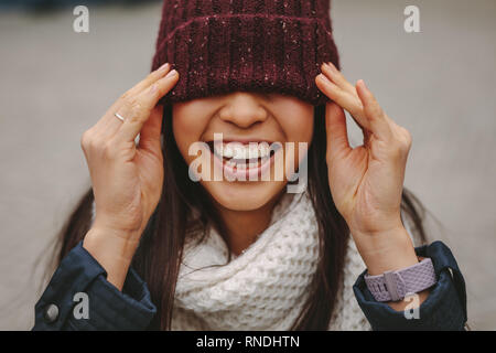 In prossimità di una donna sorridente in inverno indossare con il volto coperto con un cappuccio d'inverno. Donna sorridente che copre la sua gli occhi con un cappuccio di len. Foto Stock