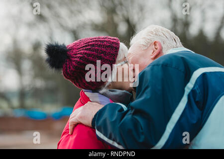 Senior l uomo sta baciando la moglie al di fuori della loro casa in inverno. Foto Stock