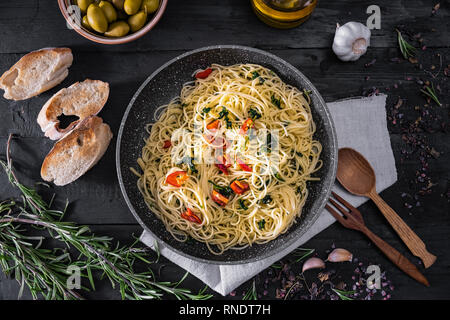 Pentola di cottura della pasta italiana, vista dall'alto. Lay piatto di spaghetti tradizionale pasto con verdure, l'aglio e olive nere su sfondo rustico Foto Stock