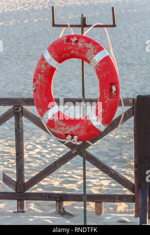 Orange salvagente con fune su un molo in legno vicino al mare. Close-up di un salvagente sul dock. mattina su di una spiaggia di sabbia Foto Stock