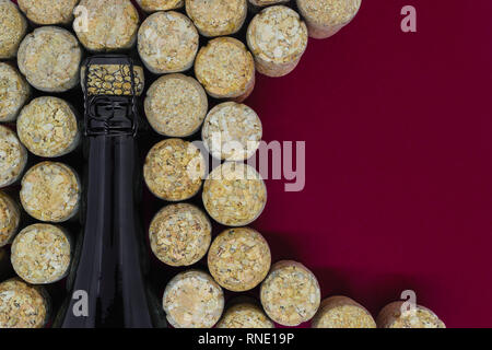 Nero bottiglia di champagne circondato di molti tappi di champagne su sfondo rosso con spazio di copia Foto Stock