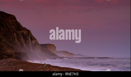 Eype, Dorset, Regno Unito. 18 febbraio 2019. Tempo nel Regno Unito: Il cielo si illumina di rosa sulle lontane scogliere di West Bay al tramonto. Credit: Notizie dal vivo di DWR/Alamy Foto Stock