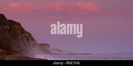 Eype, Dorset, Regno Unito. 18 febbraio 2019. Tempo nel Regno Unito: Il cielo si illumina di rosa sulle lontane scogliere di West Bay al tramonto. Credit: Notizie dal vivo di DWR/Alamy Foto Stock