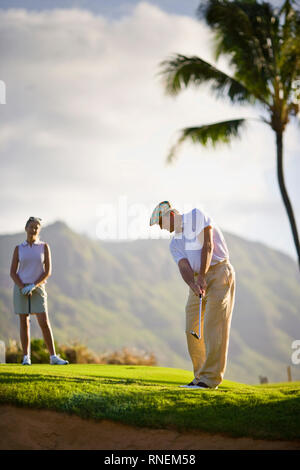 L'uomo gioca a golf come un giocatore di golf femminile guarda a. Foto Stock