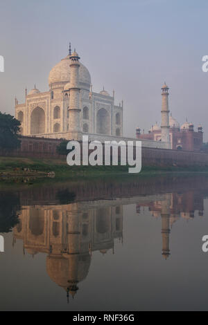 Vista del Taj Mahal con nebbia mattutina si riflette nel fiume Yamuna, Agra, Uttar Pradesh, India. Taj Mahal è stato designato come un patrimonio mondiale dell'UNESCO si Foto Stock