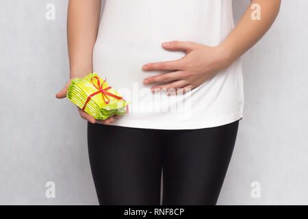 La ragazza tiene la parte inferiore dell'addome e tiene in mano una pila con assorbenti igienici per le mestruazioni, close-up, PMS, ginecologia, protettivo, napki Foto Stock