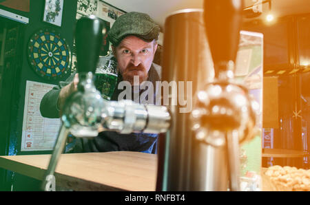 Arrabbiato e orgoglioso ragazzo irlandese tenendo la tazza di verde birra nei pub durante la St Patrick Day (filtro rappresentano bandiera irlandese) Foto Stock