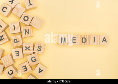 Vista superiore della media lettering con cubetti di legno su sfondo giallo Foto Stock