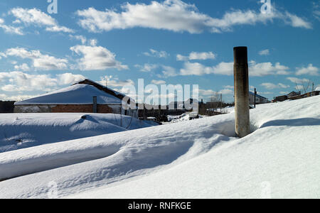 Paesaggio invernale con il cumulo di neve bianca della neve in terreno rurale su sfondo blu cielo Foto Stock