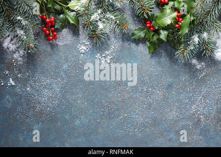 Sfondo di natale con abete e holly berry su una pietra blu sullo sfondo coperto di neve con copia spazio. Foto Stock